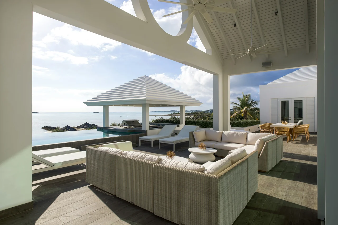 A covered terrace with white sofas over an infinity pool and the ocean