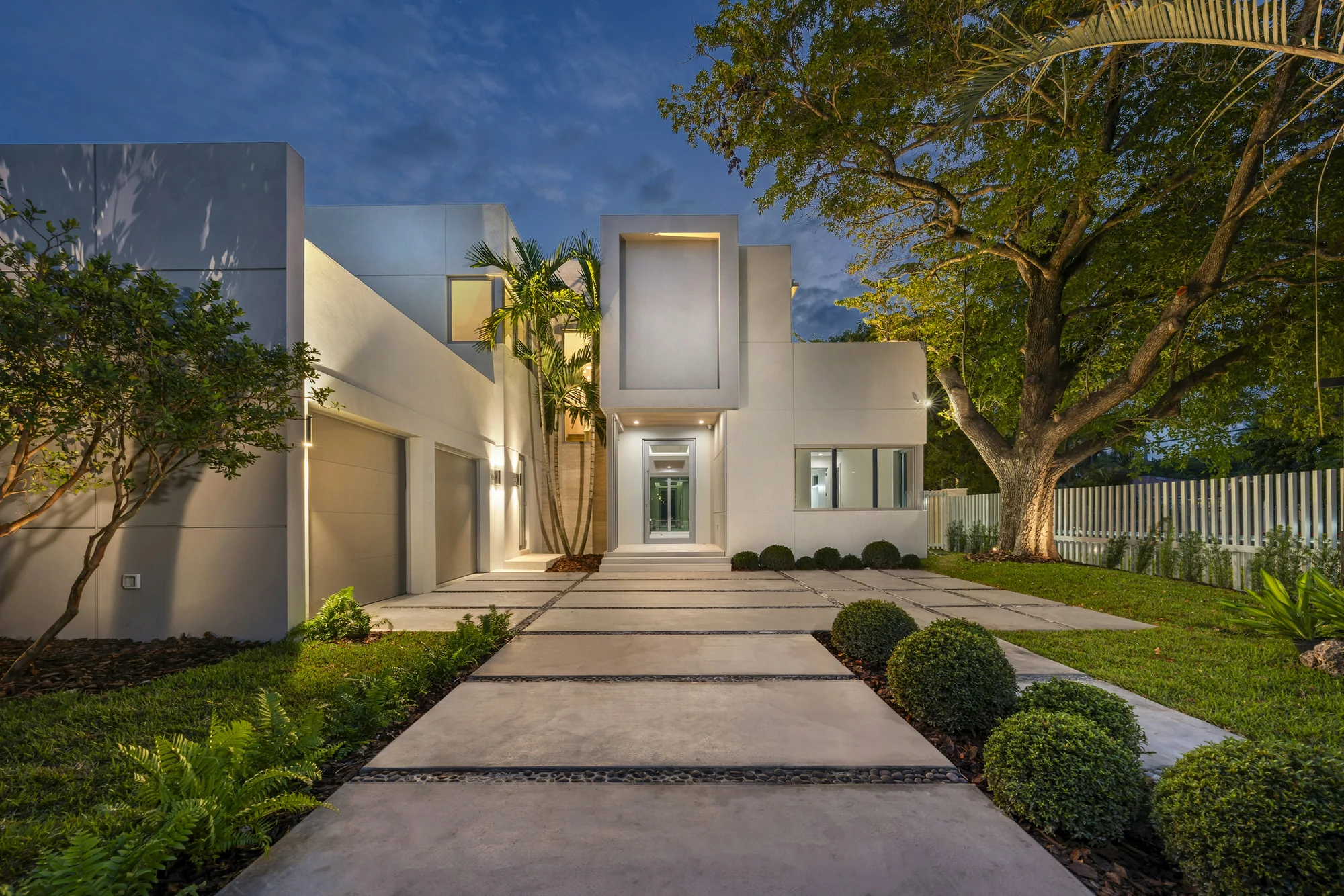 A lit path leading to a white modern house at dusk