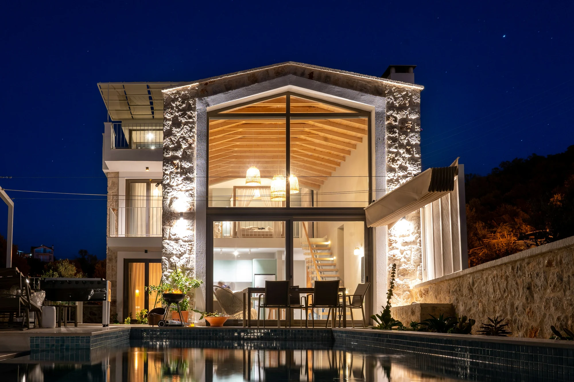 Low modern villa glowing at night behind a lit swimming pool