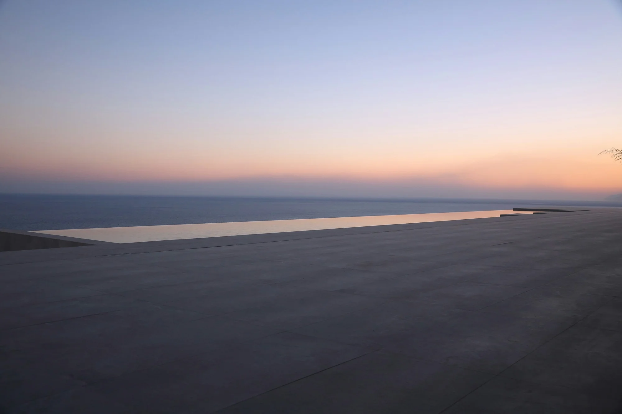 An infinity pool meeting the ocean under a sunset sky